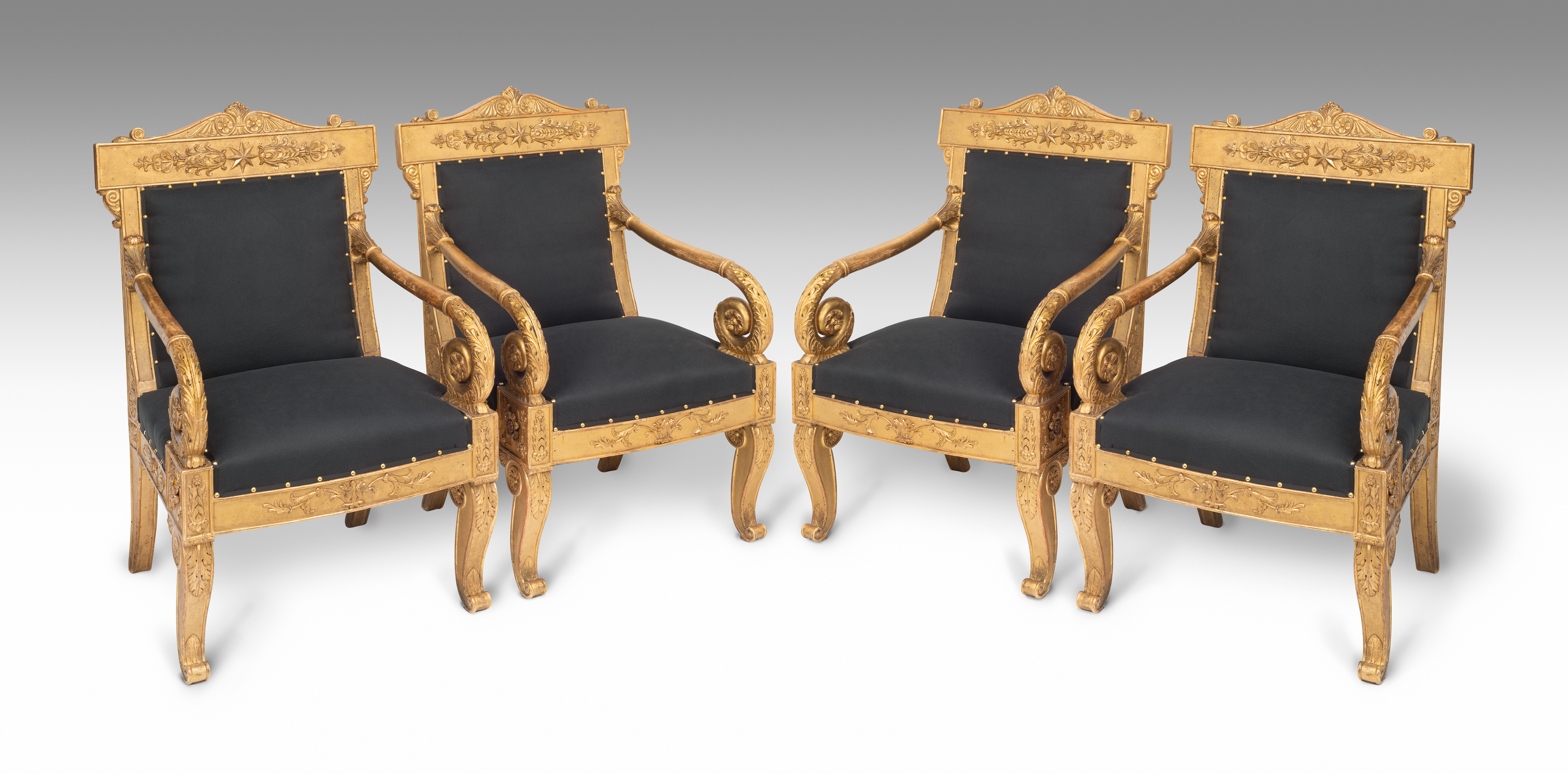 A set of four Italian walnut, carved and gilt wood and burin-finished ground (bulinato) armchairs, each with a tablet top-rail centred by a stylized foliate motif converging into an eight-point armorial star,
